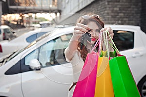 Beautiful young girl stands near a white car, makes a shopping