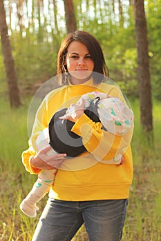 A beautiful young girl with straight dark hair in a yellow sweatshirt and jeans holds a small child in her arms in the forest at