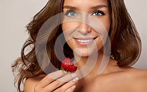 Beautiful young girl with straight white teeth smiling and eating strawberries