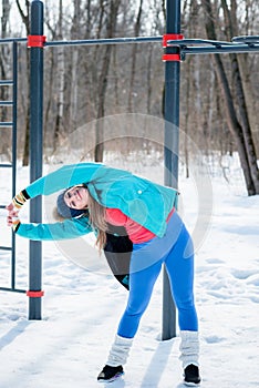 Beautiful young girl stretches on a sports field in winter again