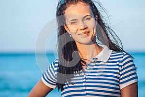 Beautiful and young girl in a striped blue dress stand against the backdrop of the blue sea and blurred beach coast line
