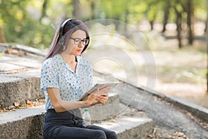 Beautiful young girl studying on a tablet on a park background. Self-education concept. Copy space.