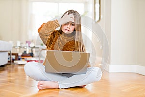 Beautiful young girl studying using laptop sitting on the floor at home stressed with hand on head, shocked with shame and