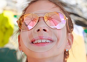 Beautiful young girl in sunglasses with beach umbrella reflection.