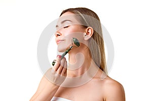 Beautiful young girl taking care after skin, doing face massage with roller isolated over white studio background