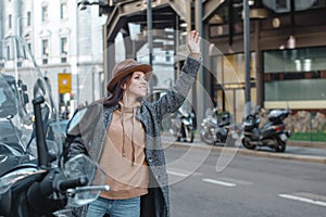 Beautiful young girl tourist on the background of the big city catches a taxi with a hand gesture.