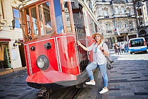 Beautiful young girl tourist in a hat poses in front of Taksim tram at popular Istiklal street in Beyoglu, Istanbul, Turkey