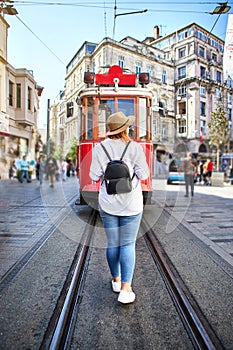 Beautiful young girl tourist in a hat poses in front of Taksim tram at popular Istiklal street in Beyoglu, Istanbul, Turkey