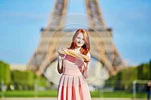 Girl with traditional French bread baguette in front of the Eiffel tower