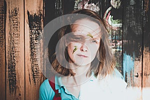 Beautiful and a young girl with an ugly hairdo on her head, stands on the background of a wooden wall which is painted in various