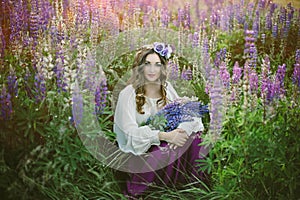 Beautiful young girl in ultra violet and white dress holding a bouquet of lupine at sunset on the field. The concept of nature and