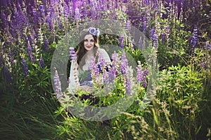 Beautiful young girl in ultra violet and white dress holding a bouquet of lupine at sunset on the field. The concept of nature and