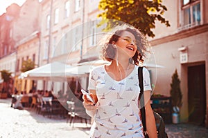 Beautiful young girl using smartphone and listening to the music walking on street. Woman dancing and singing