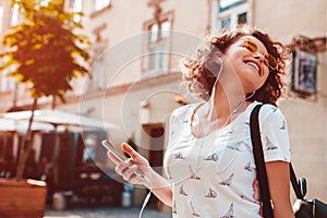 Beautiful young girl using smartphone and listening to the music walking on street. Woman dancing and singing