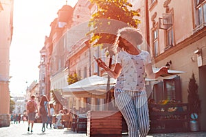 Beautiful young girl using smartphone and listening to the music walking on street. Woman dancing and singing