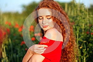 Beautiful young girl with very long red hair. Poppy field. Close-up. The concept of health, nature, cosmetics and care