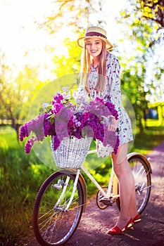 Beautiful young girl with vintage bicycle and flowers on city background in the sunlight outdoor.