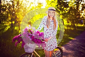 Beautiful young girl with vintage bicycle and flowers on city background in the sunlight outdoor.