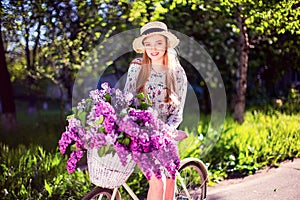 Beautiful young girl with vintage bicycle and flowers on city background in the sunlight outdoor.