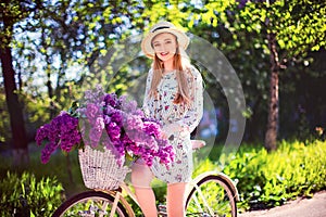 Beautiful young girl with vintage bicycle and flowers on city background in the sunlight outdoor.