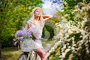 Beautiful young girl with vintage bicycle and flowers on city background in the sunlight outdoor.