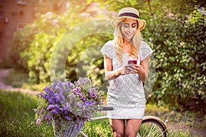 Beautiful young girl with vintage bicycle and flowers on city background in the sunlight outdoor.