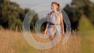 Beautiful young girl walking on the field with tall grass in the rays of the setting sun