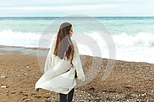 A beautiful young girl walks along the seashore, a storm, hair fly apart, a gray cardigan, a sports figure in sneakers