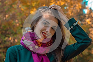 Beautiful young girl in a warm scarf keeps your hand for hair and smiling close-up