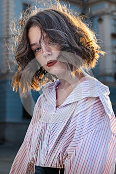 Beautiful young girl with wavy hair, red lips and freckles dressed in white striped shirt looking at the camera