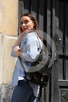 Beautiful young girl wearing blue jeans, shirt and white t-shirt posing with black leather backpack