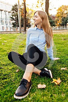 Beautiful young girl, wearing business clothes, smiling and enjoying a warm day, sitting on a green lawn