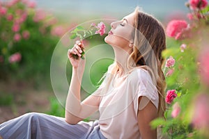 Beautiful young girl is wearing casual clothes having rest in a garden with pink blossom roses