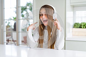 Beautiful young girl wearing headphones listening to music and dancing very happy pointing with hand and finger