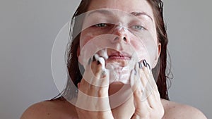 Beautiful young girl with wet hair in the shower. Young red hair happy woman applying foam for washing on her face