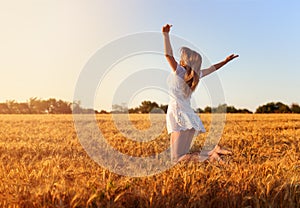 Beautiful young girl in white dress jumping in golden wheat