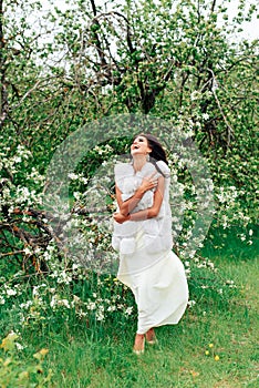 Beautiful young girl in white dress in spring blossoming apple orchards