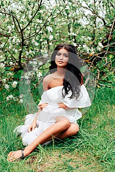 Beautiful young girl in white dress in spring blossoming apple orchards