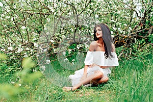 Beautiful young girl in white dress in spring blossoming apple orchards