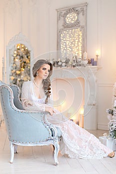 Beautiful young girl in a white lace negligee in a bright interior with a fireplace