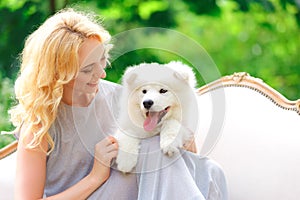 Beautiful young girl with a white puppy in her arms on a retro sofa in a summer garden