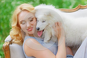 Beautiful young girl with a white puppy in her arms on a retro sofa in a summer garden