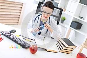 A beautiful young girl in a white robe sits at a computer desk, holds a marker in her hand and opens a bottle of water.