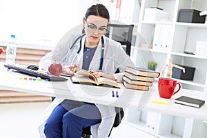 A beautiful young girl in a white robe sits at a computer desk, holds a marker and a pen in her hand and looks at the