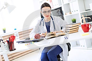 A beautiful young girl in a white robe sits at a computer desk, holds a marker and a pen in her hand and looks at the