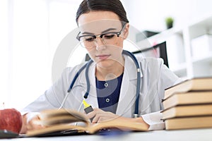 A beautiful young girl in a white robe is sitting at the computer desk with a marker and a book. A photograph with a