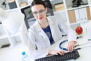 A beautiful young girl in a white robe is sitting at the table and typing on the keyboard.