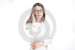 Beautiful young girl in a white shirt on white isolated background talking on a mobile phone. Smiles portrait to the