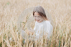 Beautiful young girl in a white sweater sits in a wheat field and smiles cheerfully