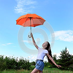 beautiful young girl white T-shirt and denim shorts holds orange umbrella high above her head. Walk sunny summer day open air